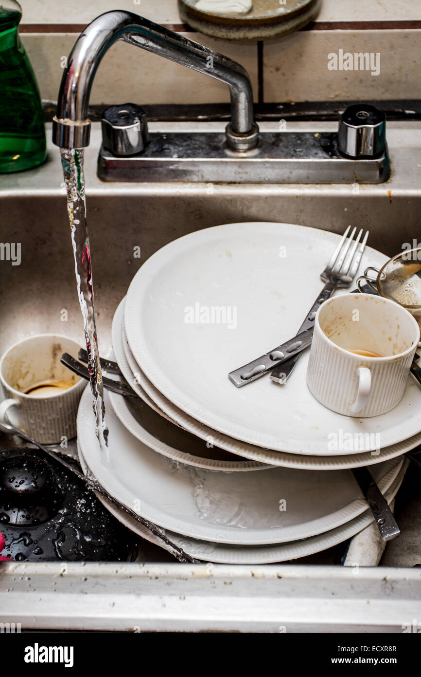 Dirty dishes at the kitchen sink waiting to be washed while the tap is  running Stock Photo - Alamy