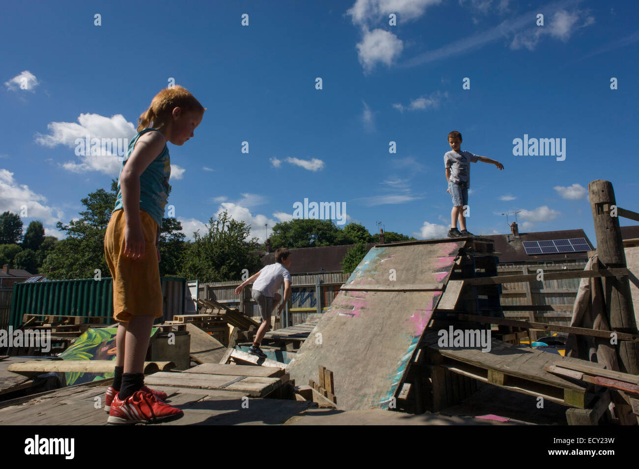 Children play on old crates and pallets in risk averse playground called The Land on Plas Madoc Estate, Ruabon, Wrexham, Wales. Stock Photo