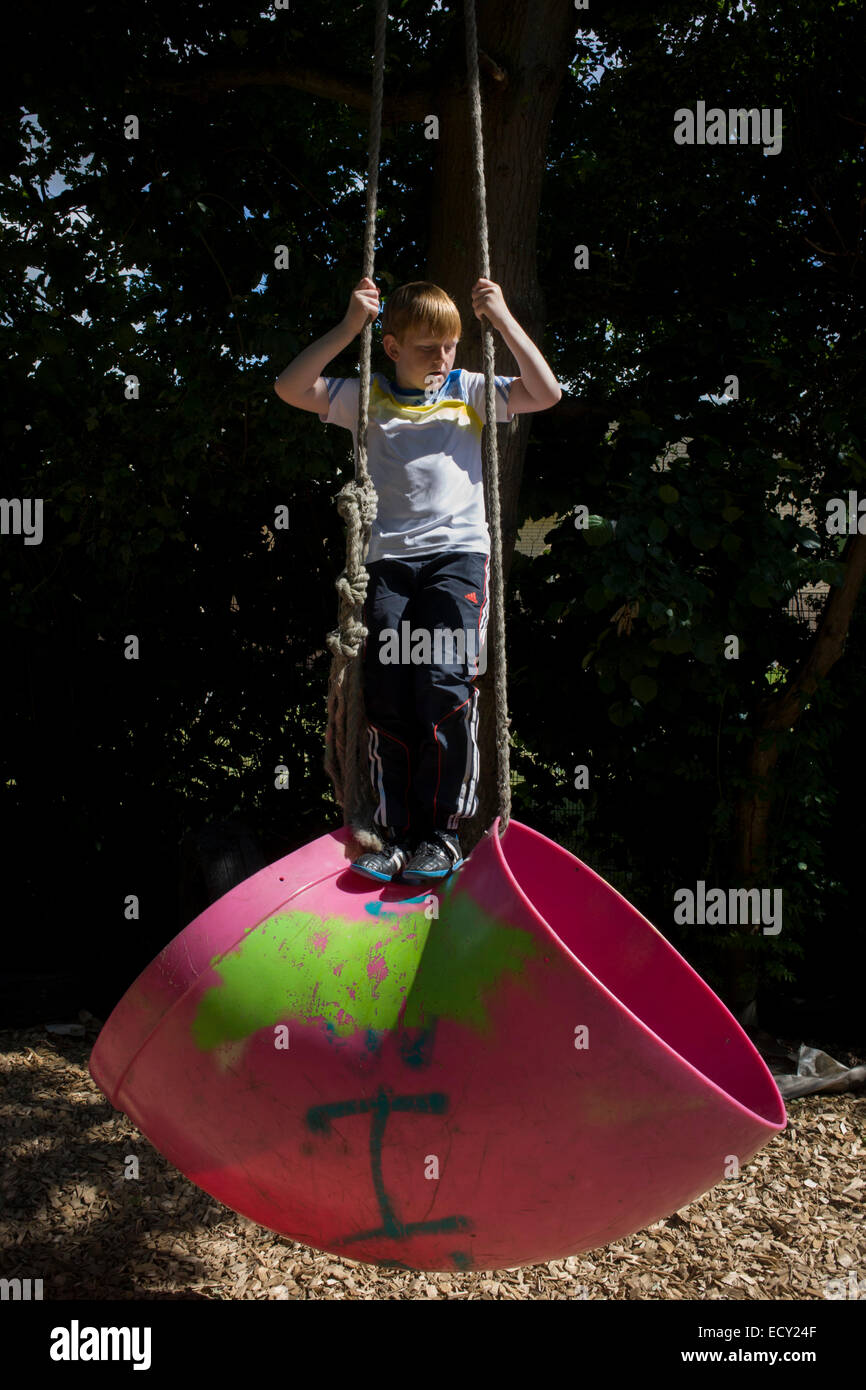 Boy swings on rope in risk averse playground called The Land on Plas Madoc Estate, Ruabon, Wrexham, Wales. Stock Photo