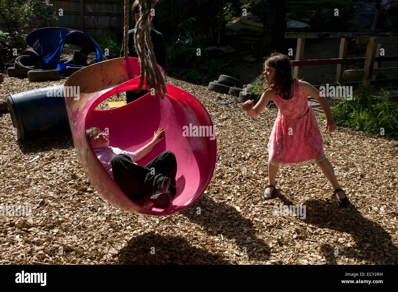 Children play with rope swing in risk averse playground called The Land on Plas Madoc Estate, Ruabon, Wrexham, Wales. Stock Photo