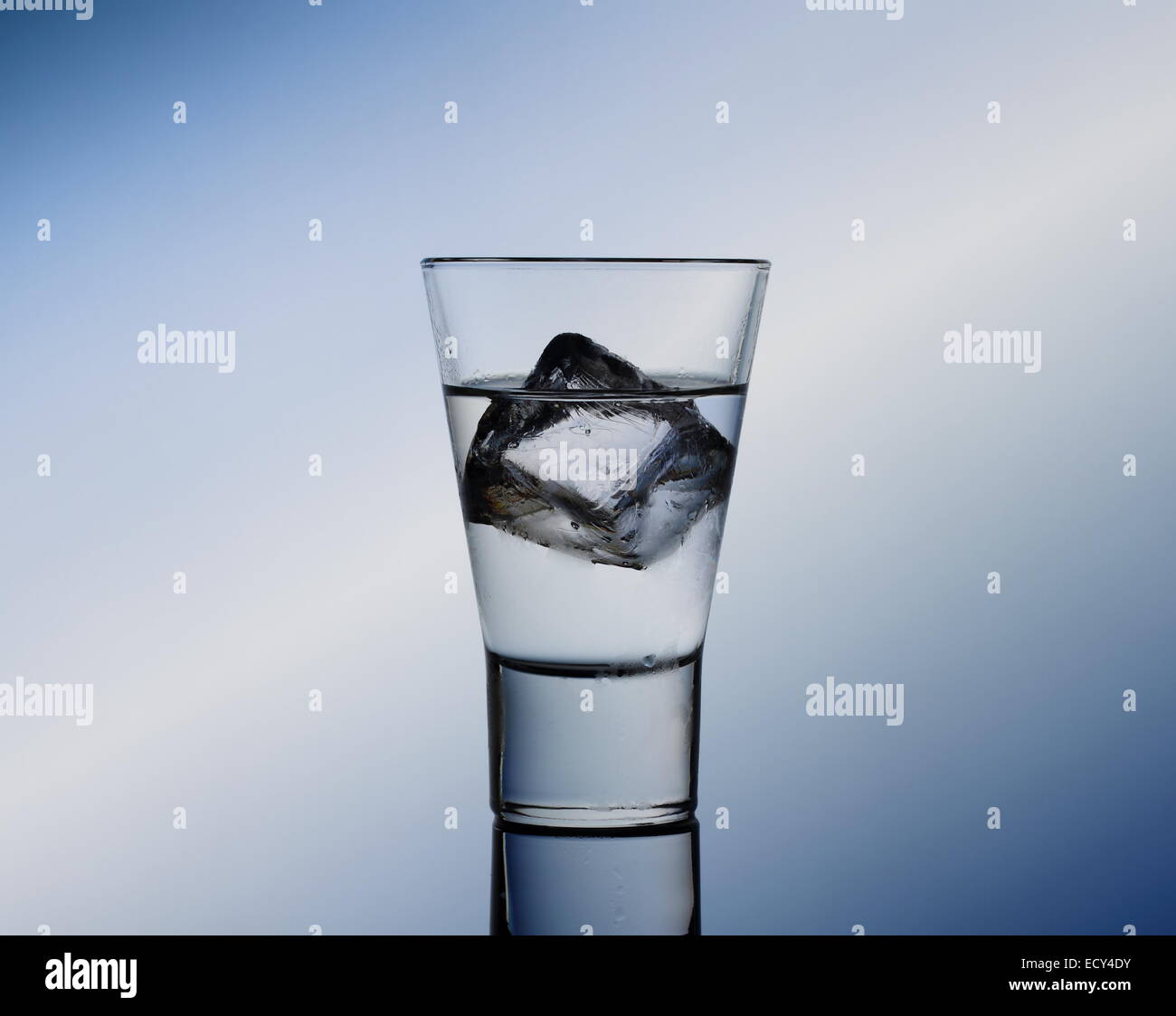 Short drink glass with clear liquid and ice cubes, blue background Stock Photo