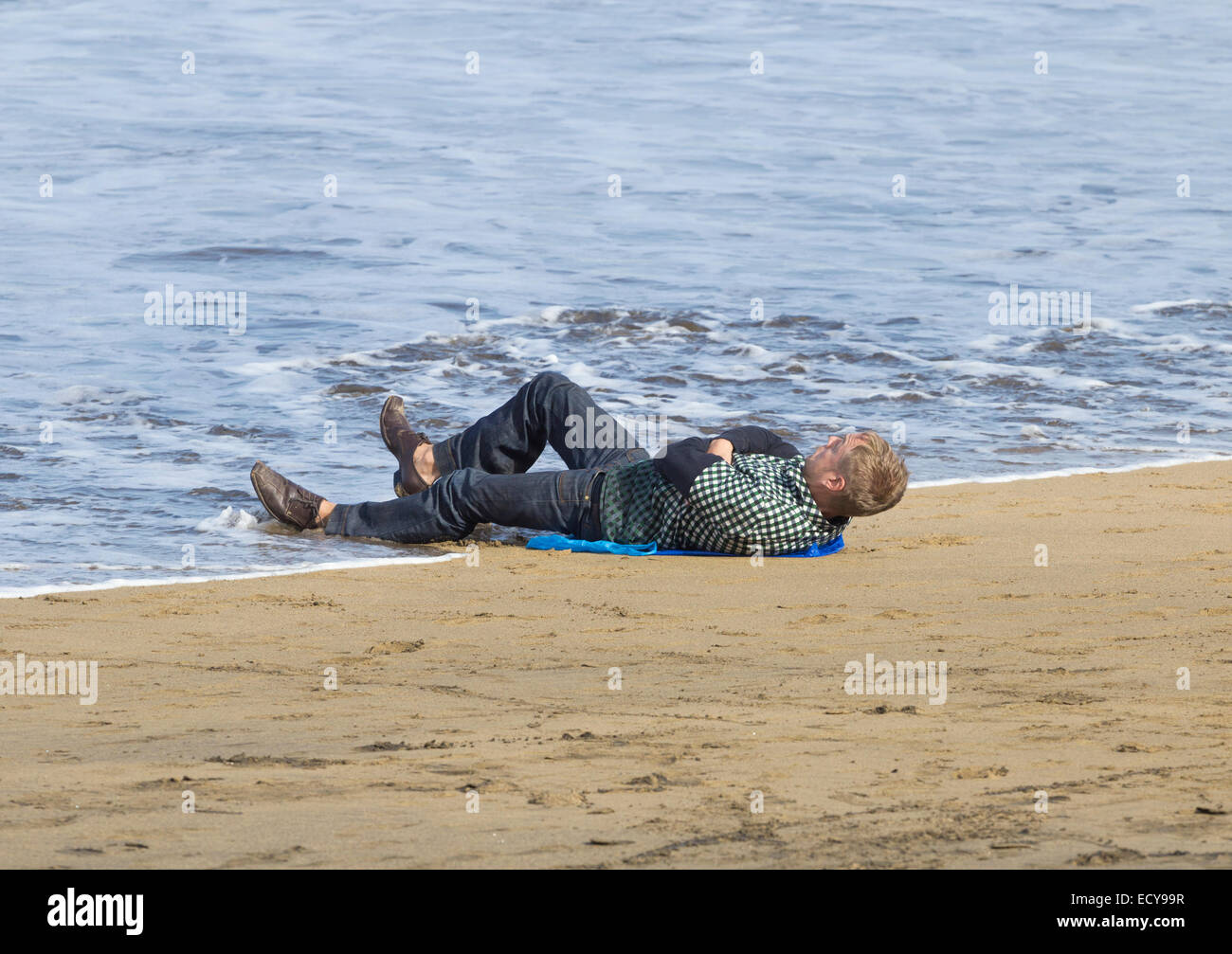 Man snoozing on beach is soaked by the incoming tide. Stock Photo