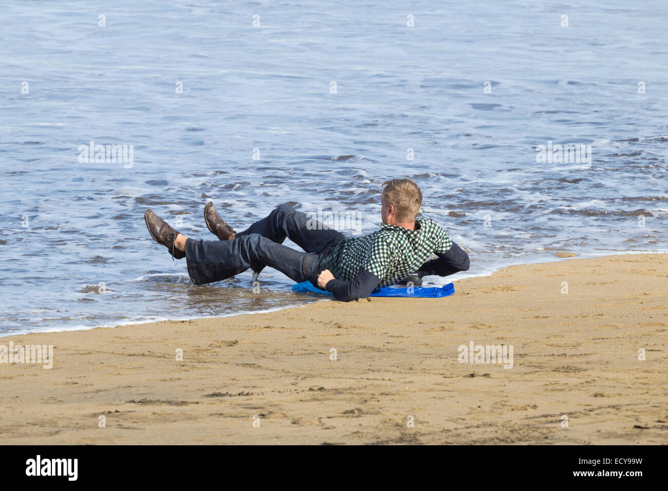 Man snoozing on beach is soaked by the incoming tide. Stock Photo