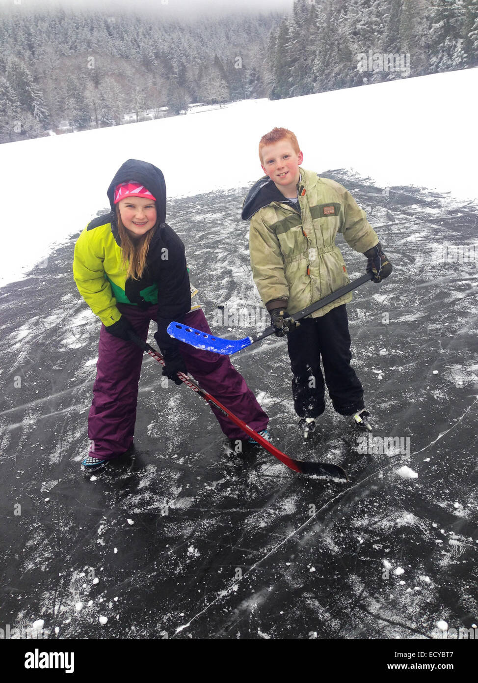 Caucasian children playing hockey on ice covering frozen lake - Smartphone Captured Stock Image