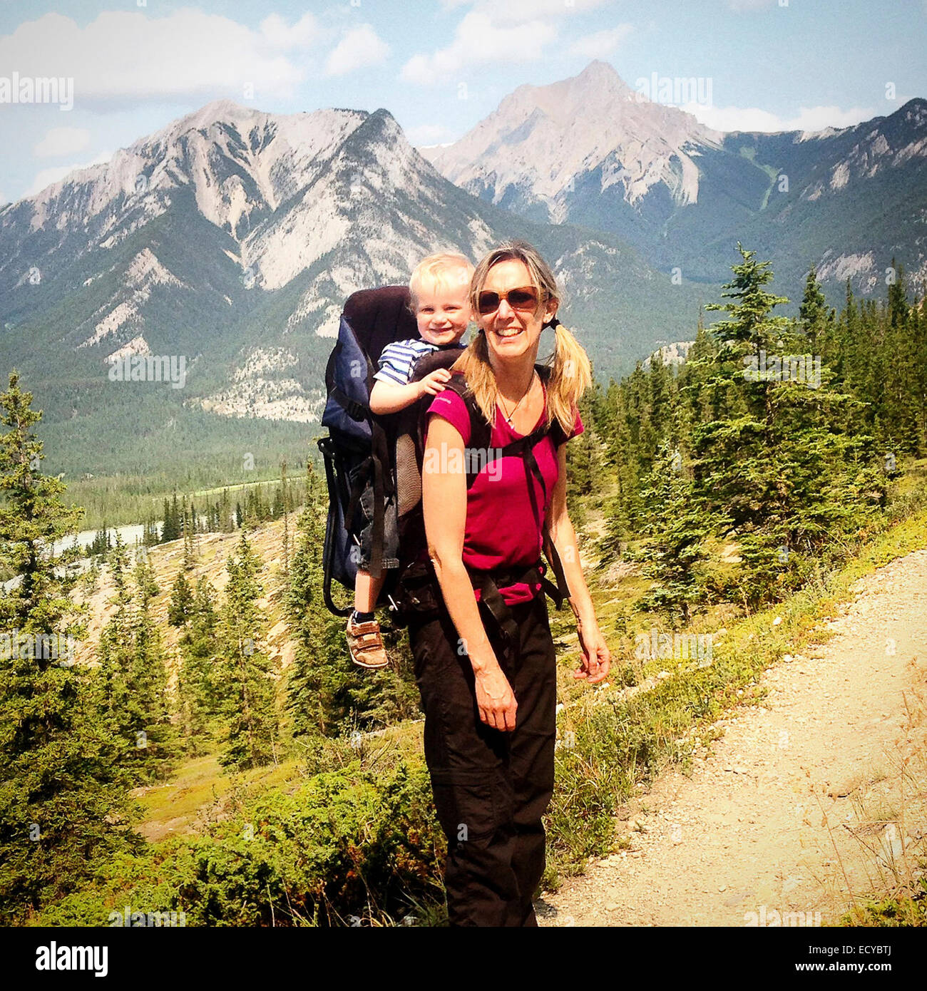 Hiker carrying son in backpack on mountain trail - Smartphone Captured Stock Image