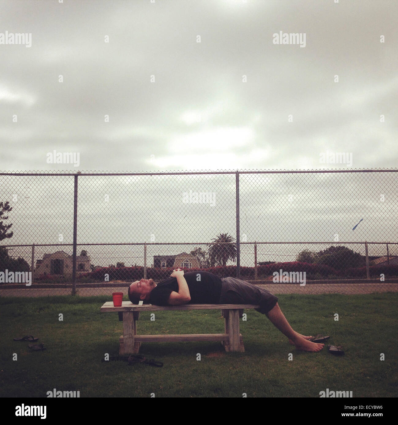 Caucasian man laying on bench in park - Smartphone Captured Stock Image