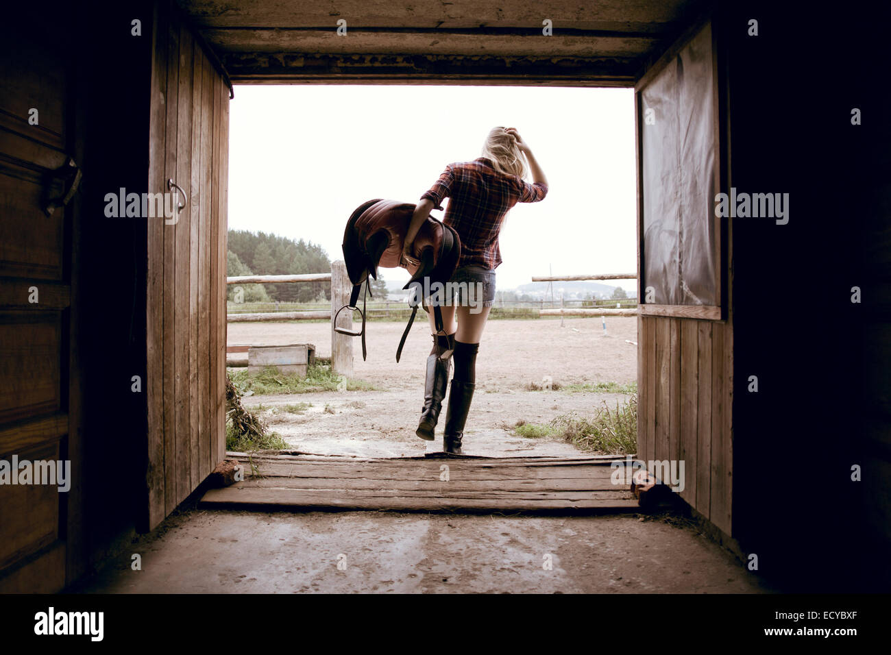 Caucasian woman carrying horse saddle in barn doorway Stock Photo Alamy