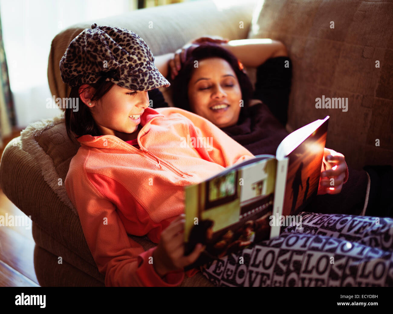 Mother and daughter reading book on sofa Stock Photo