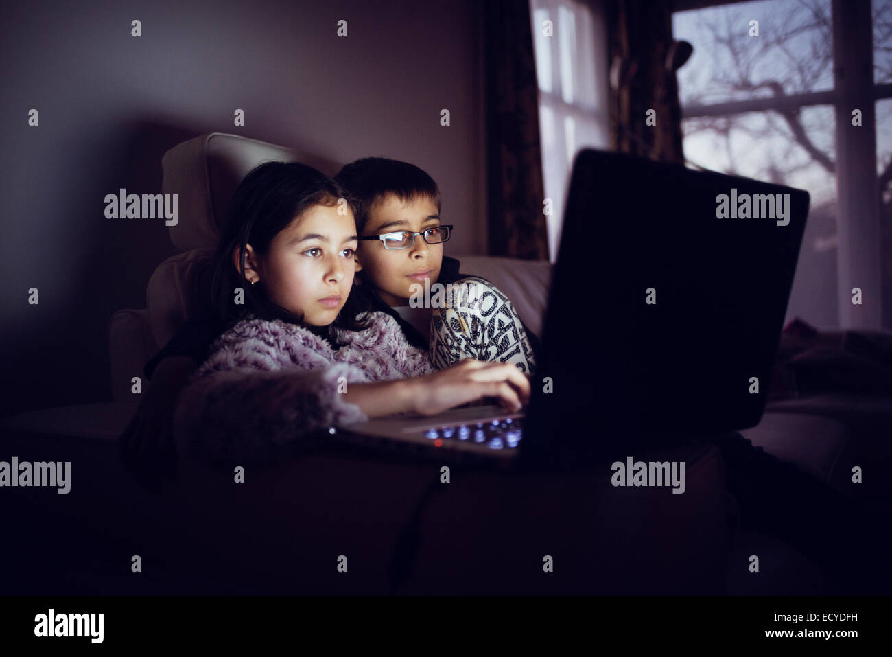 Mixed race sisters using laptop at night Stock Photo