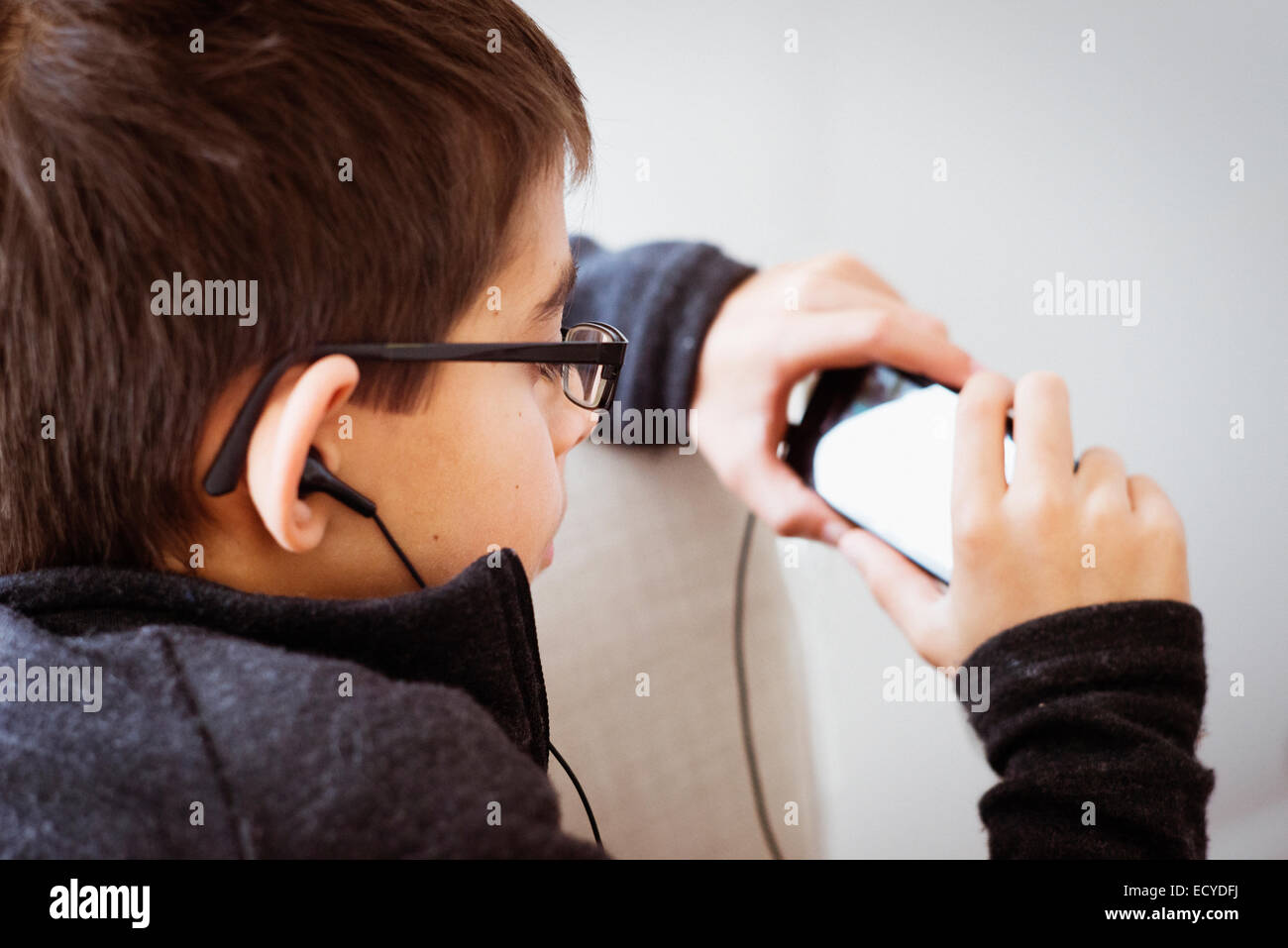 Mixed race boy listening to earbuds and using cell phone Stock Photo