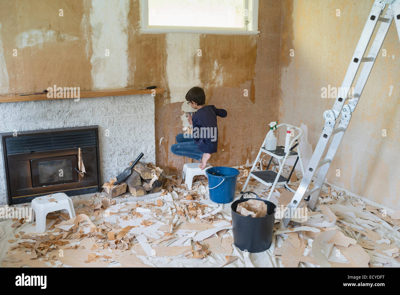 Mixed race boy stripping wallpaper in living room Stock Photo