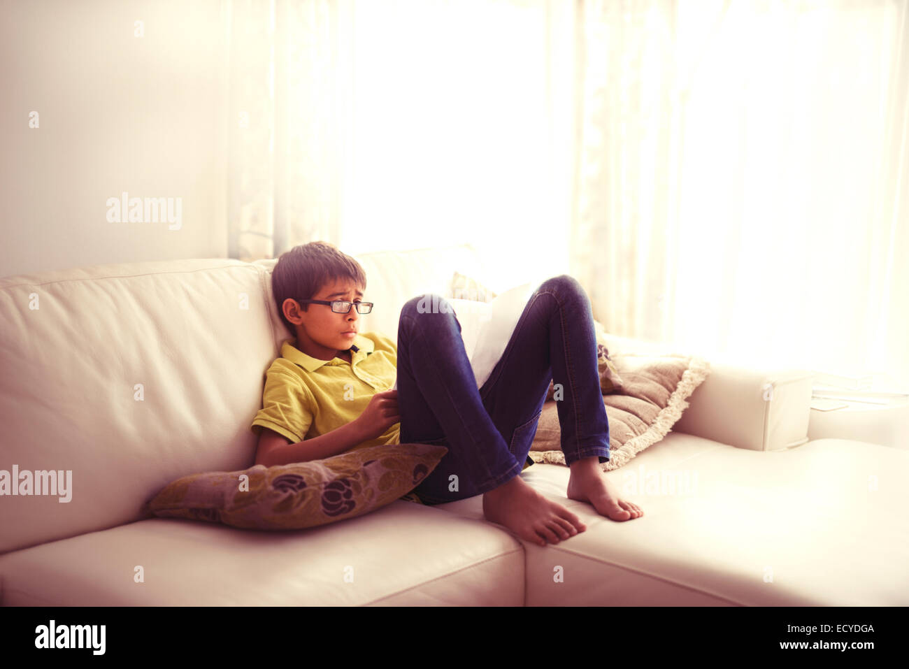 Mixed race boy reading book on living room sofa Stock Photo