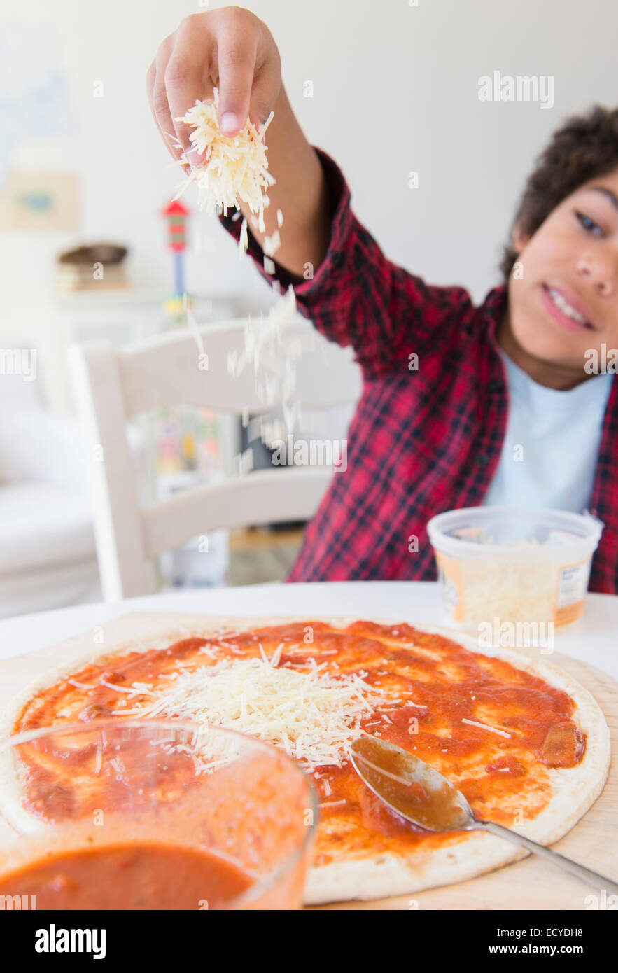 Mixed race boy sprinkling cheese on homemade pizza Stock Photo