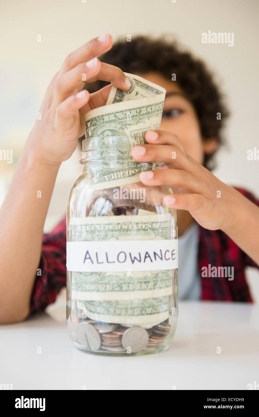 Mixed race boy putting allowance in savings jar Stock Photo