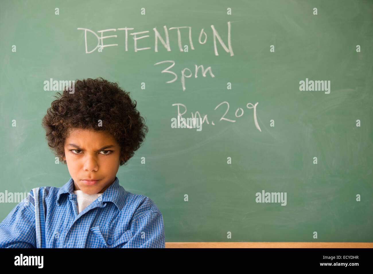 Angry mixed race boy frowning in classroom detention Stock Photo