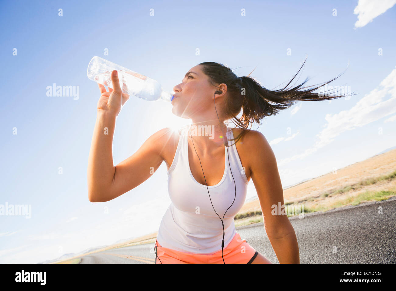 Caucasian runner drinking water bottle on remote road Stock Photo