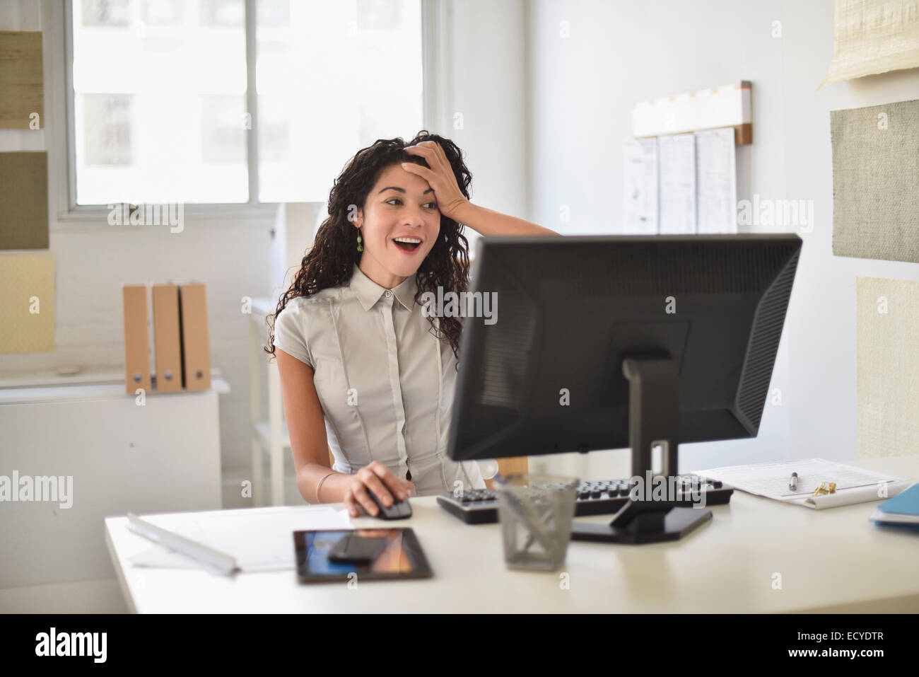 Mixed race businesswoman gasping at computer at desk in office Stock Photo