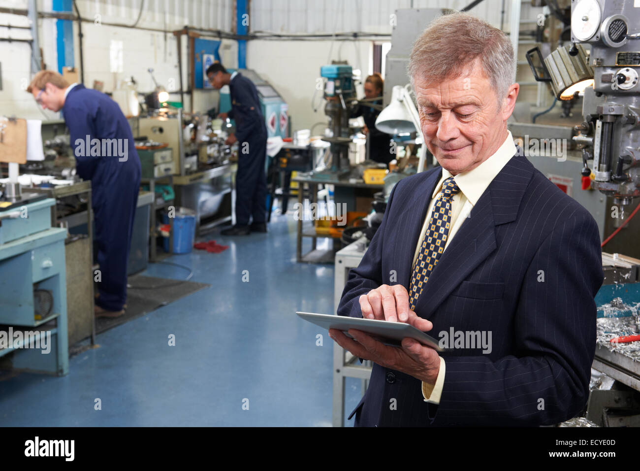 Owner Of Engineering Factory Using Digital Tablet With Staff In Background Stock Photo