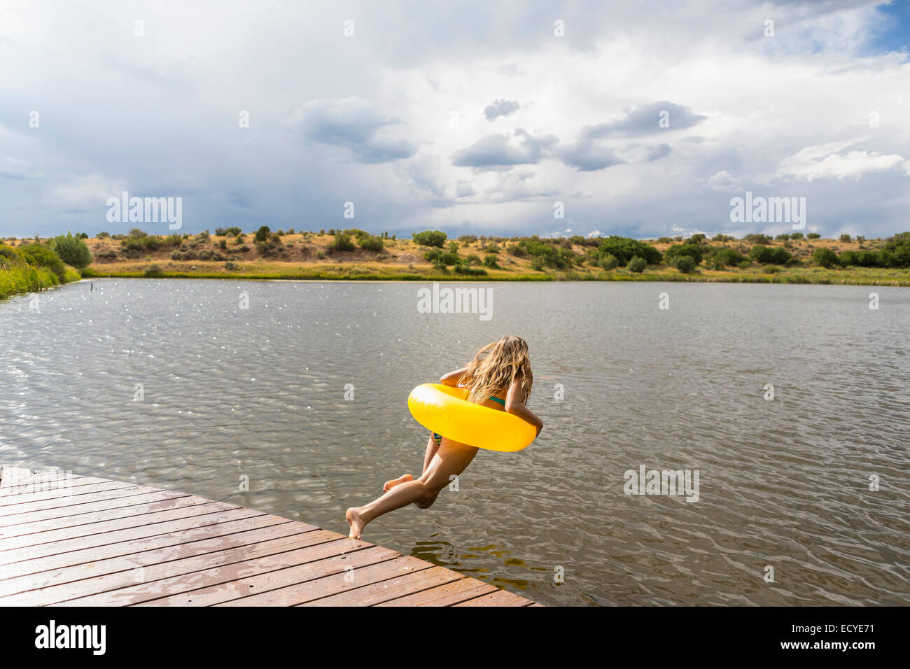 Mixed race teenage girl in inflatable ring jumping into still lake Stock Photo