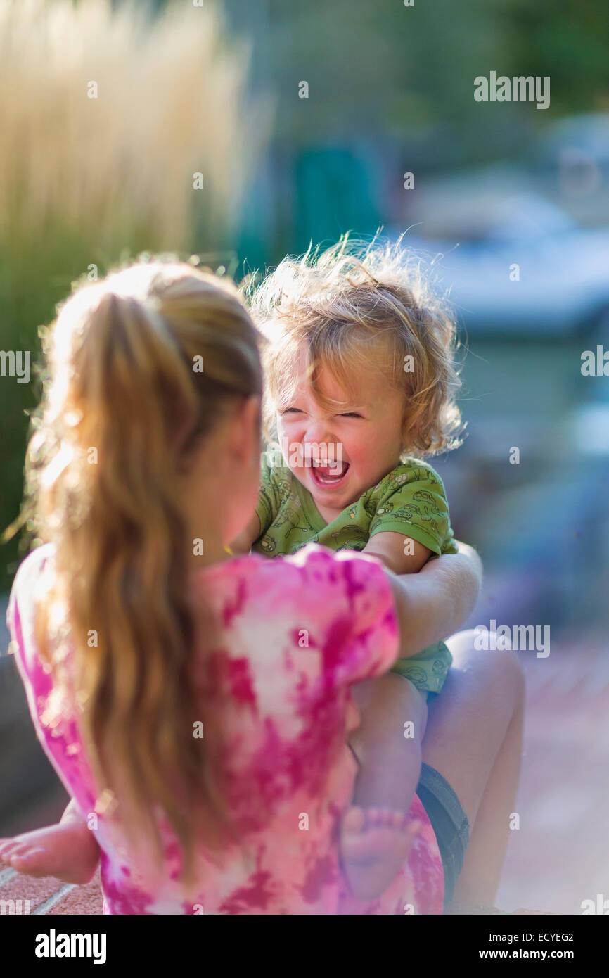 Caucasian sister holding laughing baby brother outdoors Stock Photo