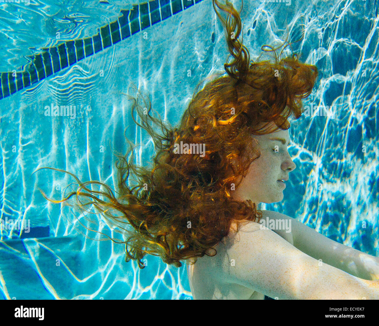 Teenage girl with red hair swimming underwater in pool Stock Photo