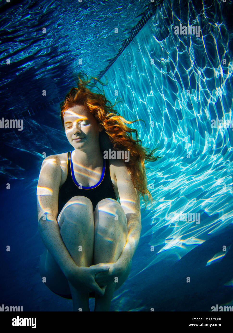 Teenage girl with red hair swimming underwater in pool Stock Photo