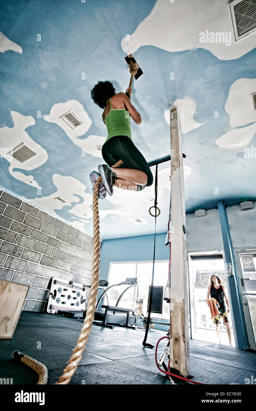 African American woman climbing rope in gym Stock Photo