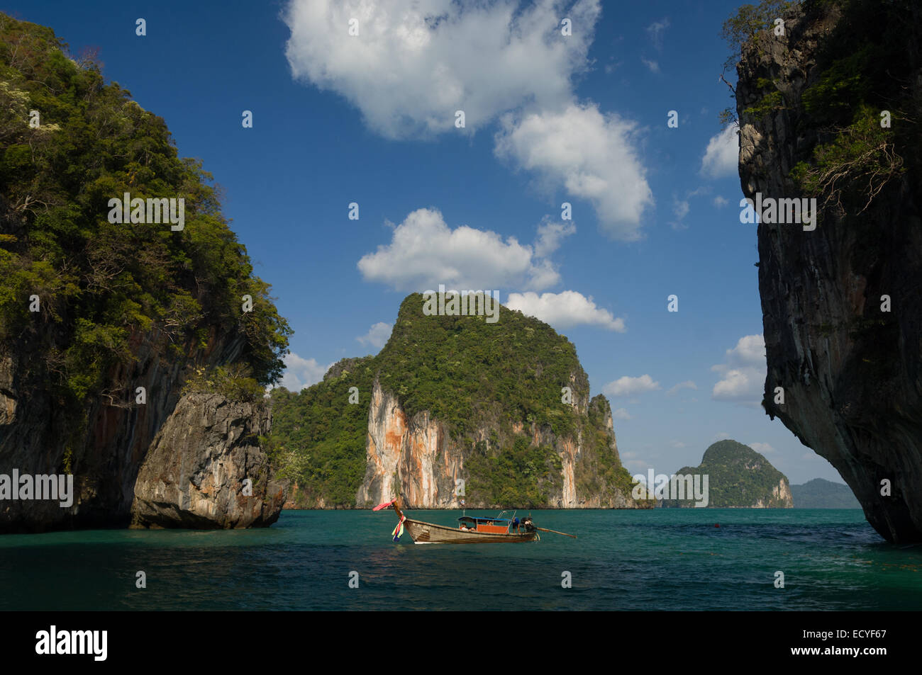 Tourists in a traditional Thai longtail fishing boat, moored between limestone rock formations, Phang Nga Bay, near Krabi, Thailand Stock Photo