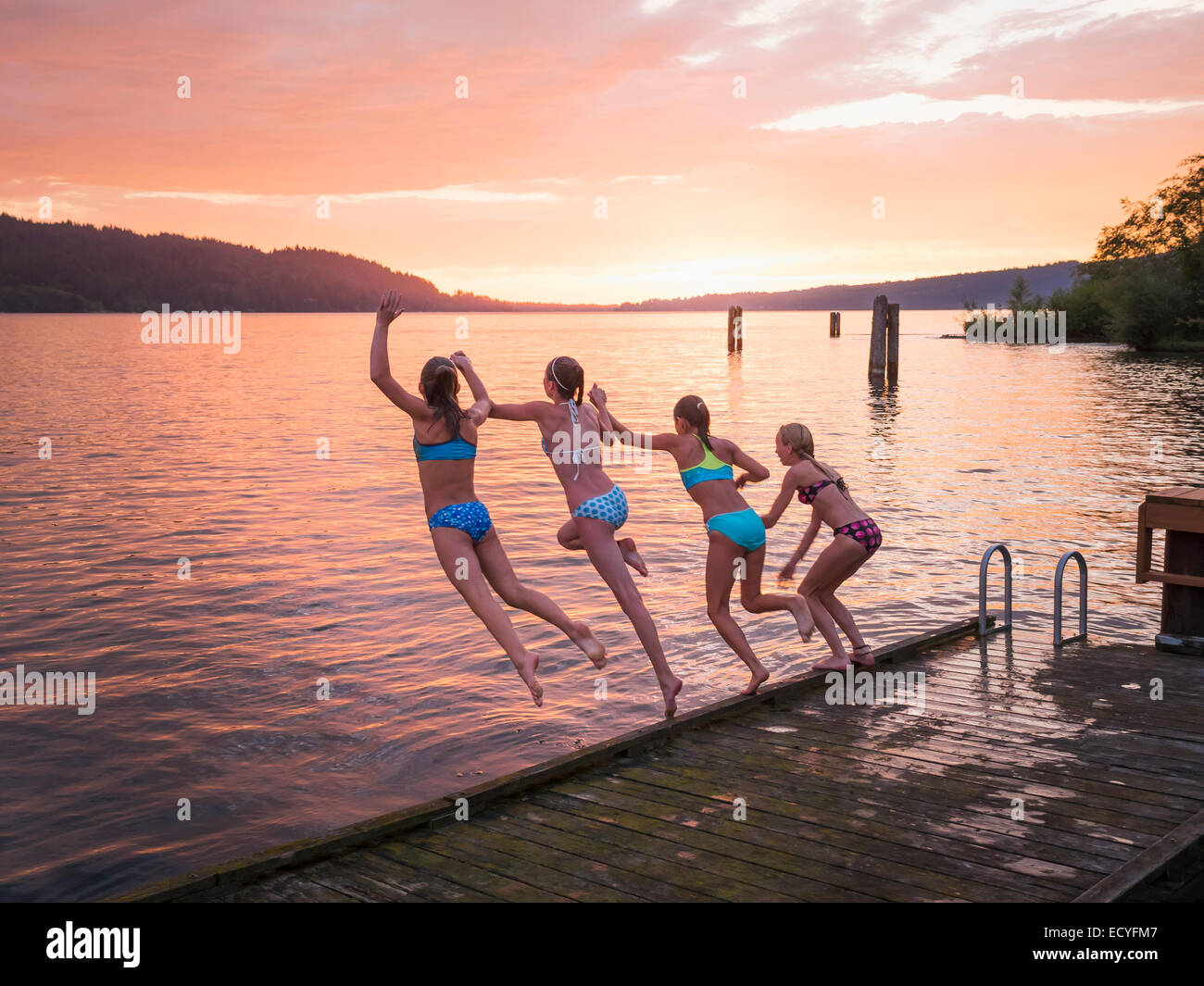 Girls jumping into lake from wooden dock Stock Photo