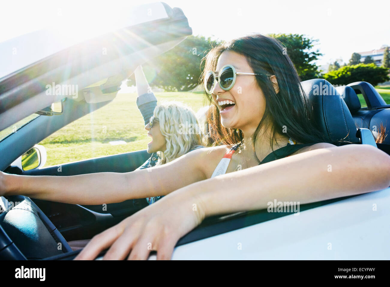 Excited women driving convertible on road trip Stock Photo