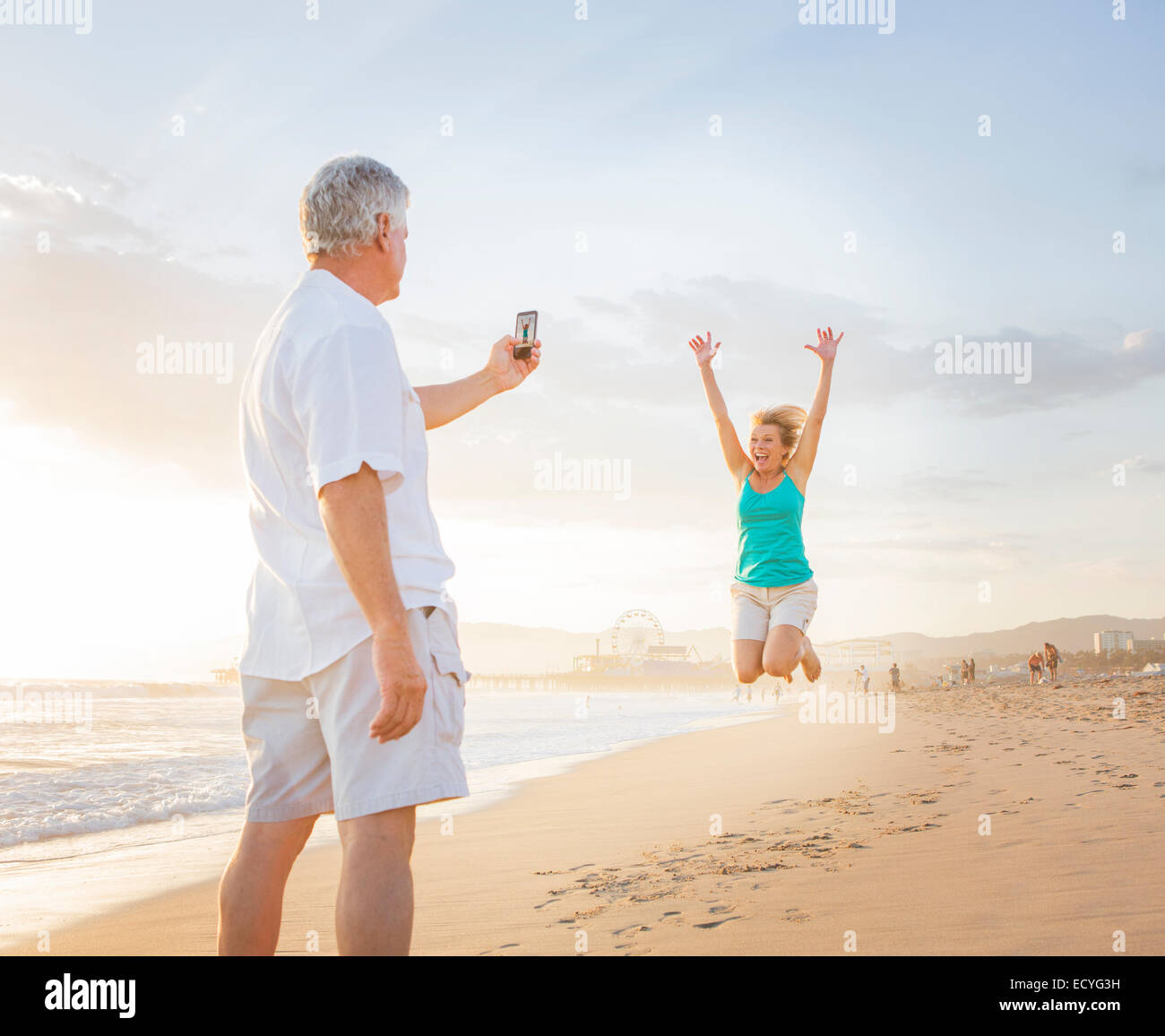 Caucasian man taking cell phone photograph of wife on beach Stock Photo