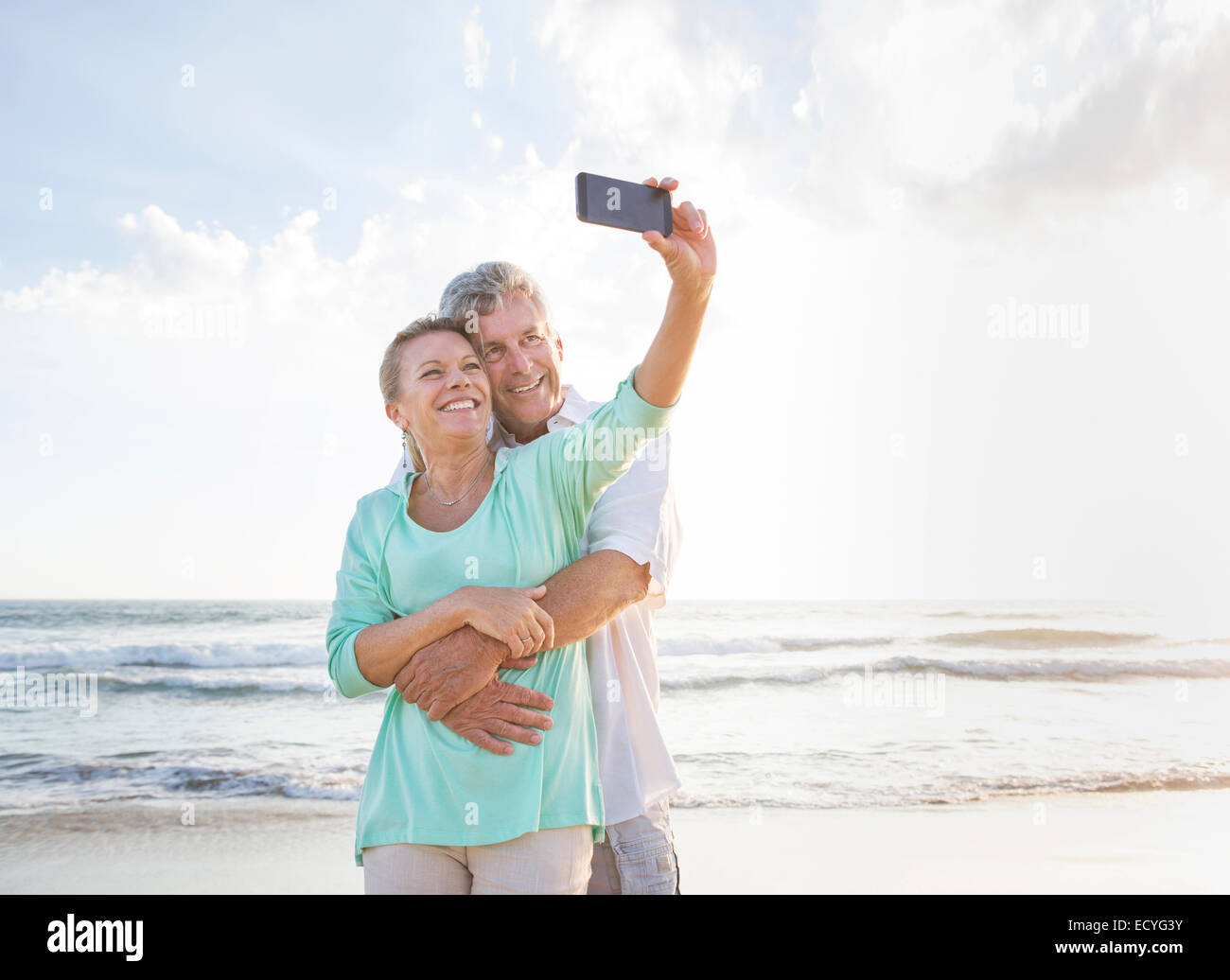 Caucasian couple taking cell phone selfie on beach Stock Photo