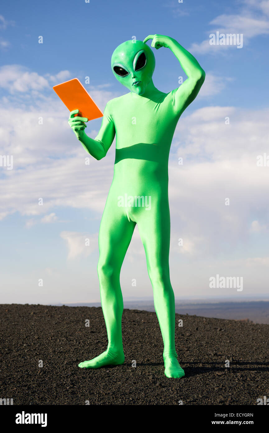Confused green alien scratching head looking down at orange tablet Stock Photo