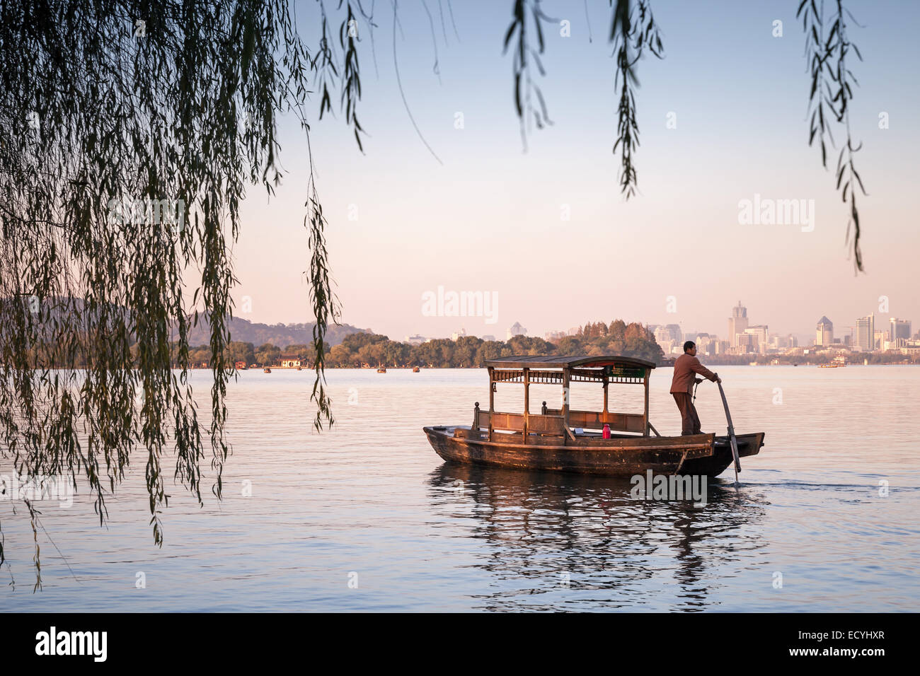 Hangzhou, China - December 5, 2014: Traditional Chinese wooden recreation boat with boatman floats on the West Lake. Famous park Stock Photo