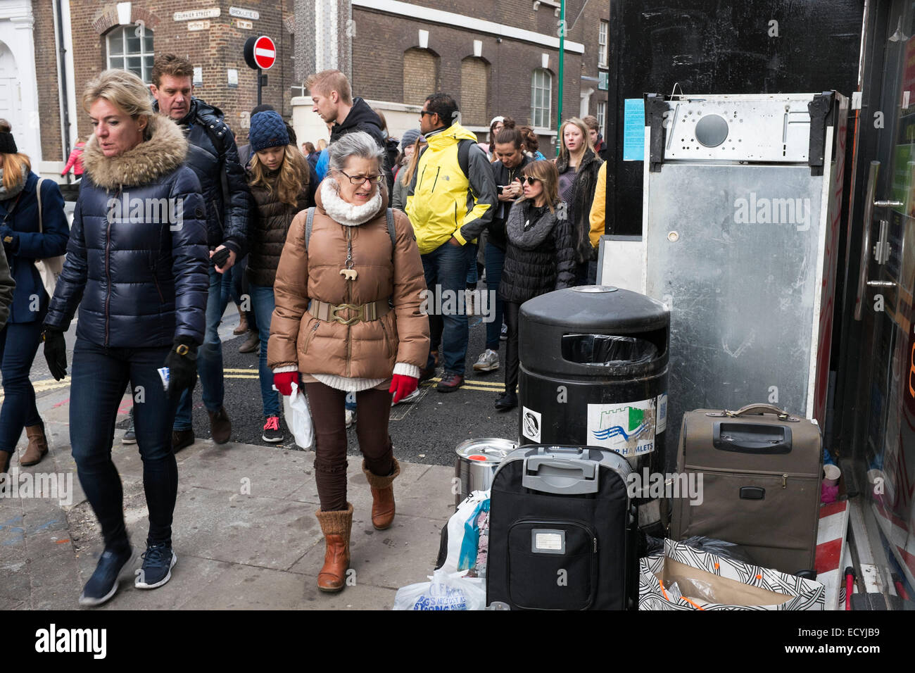 Street scene at Brick Lane Market in the East End of London, UK. A tour group looks and grimaces at waste left by a rubbish bin. Stock Photo