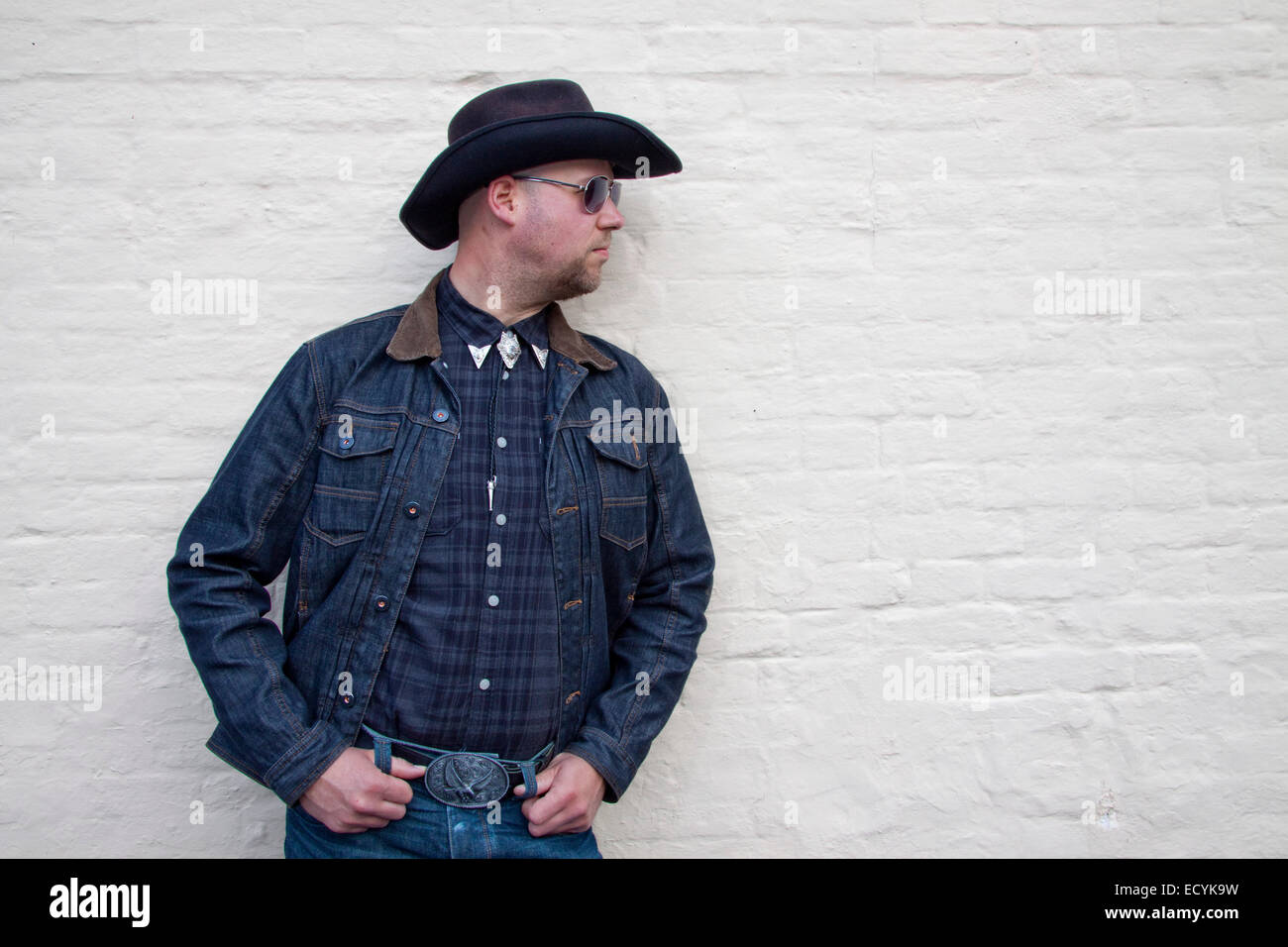 A young man dressed as a cowboy and wearing sunglasses poses in a macho ...