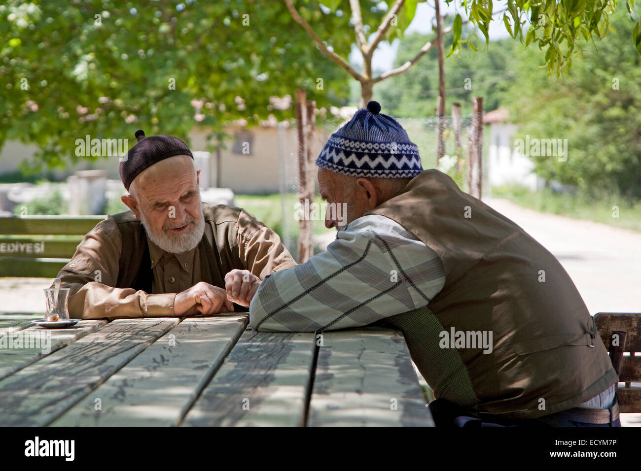 Two bearded elderly men wearing traditional taqiyah having a cup of tea on the main square of a small village in western Turkey Stock Photo