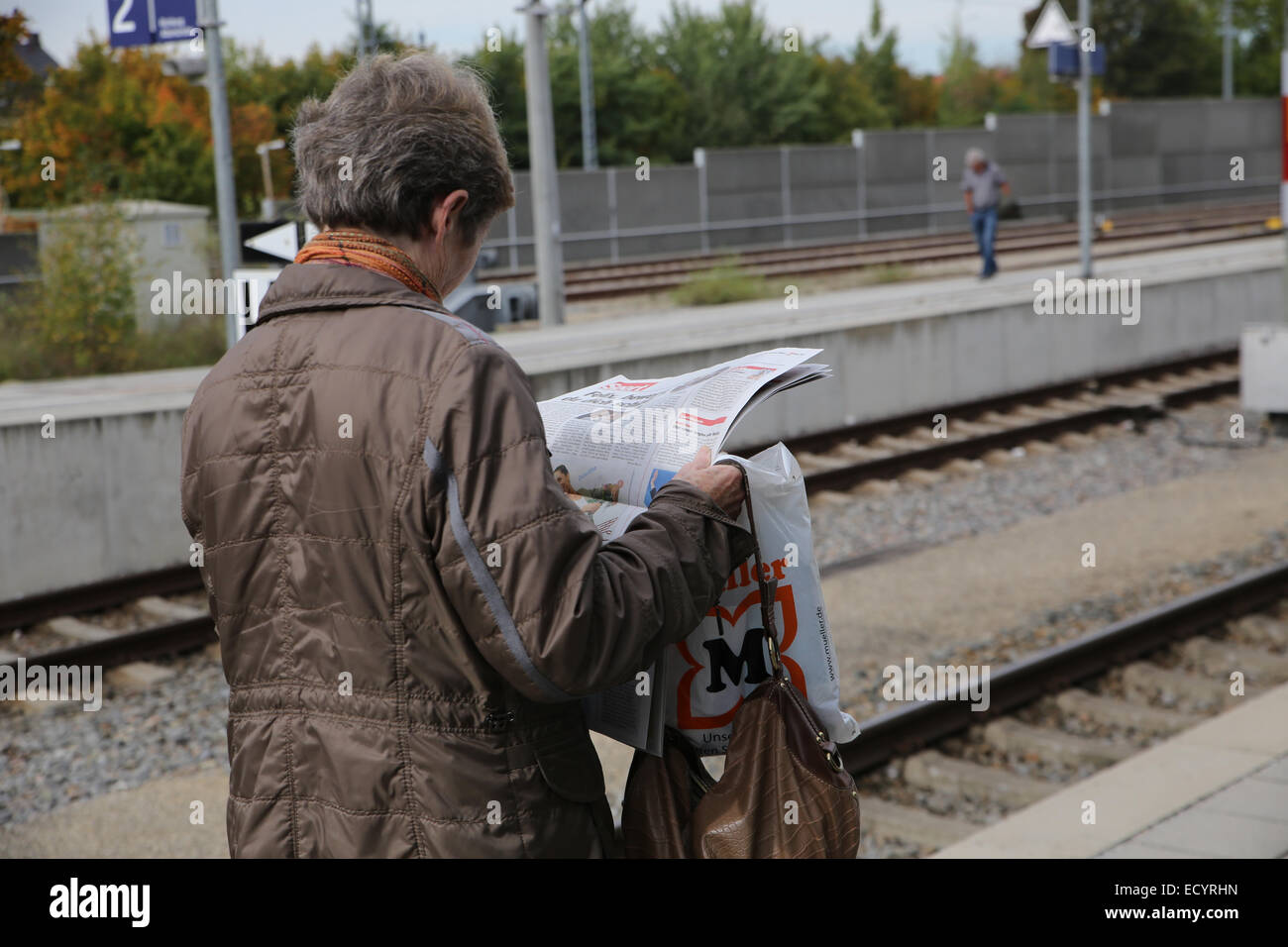 woman reading newspaper waiting train station Stock Photo