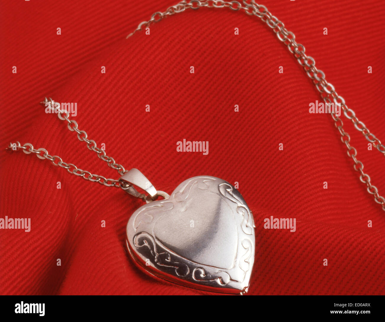 Ladies silver locket on chain against red material. Stock Photo
