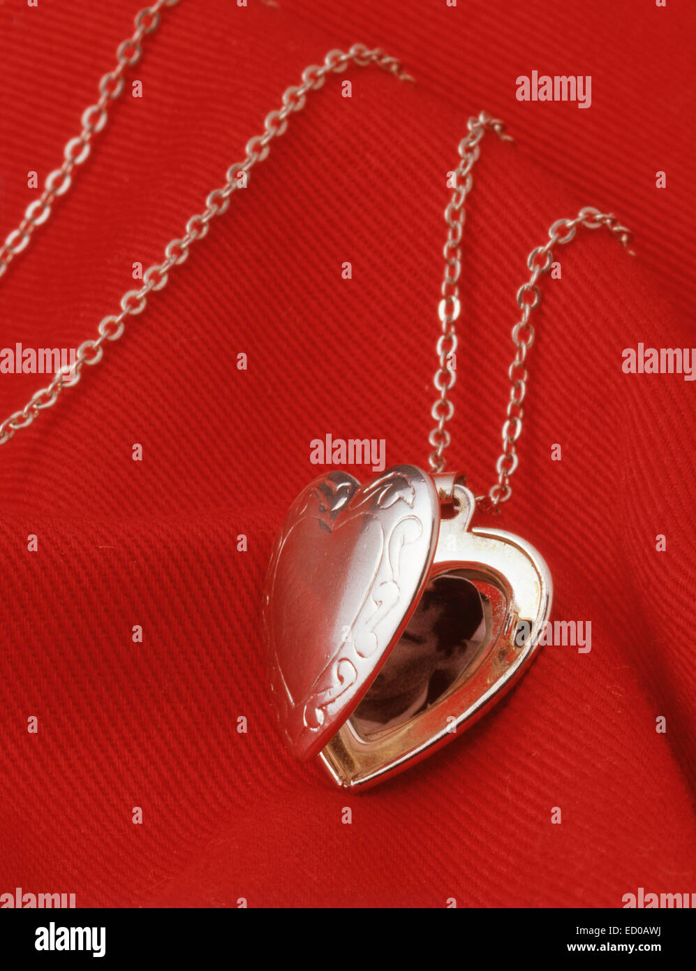 Ladies silver locket on chain against red material. Stock Photo