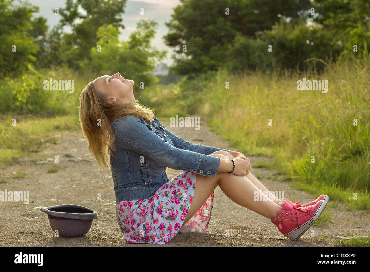 Blonde girl (14-15) sitting on dirt road and laughing Stock Photo - Alamy