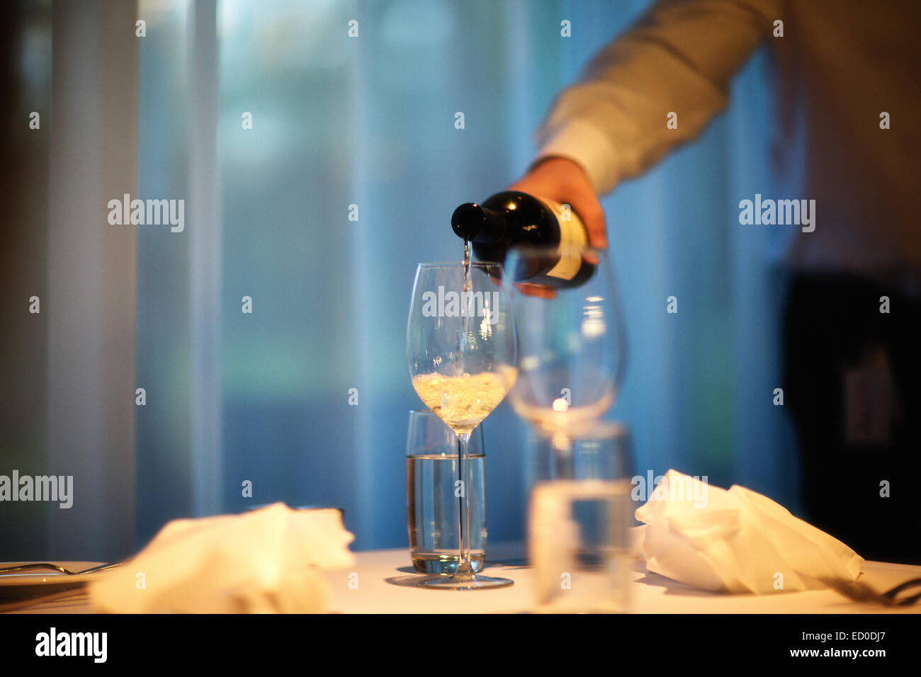 Cropped shot of man in room pouring white wine in wineglass Stock Photo
