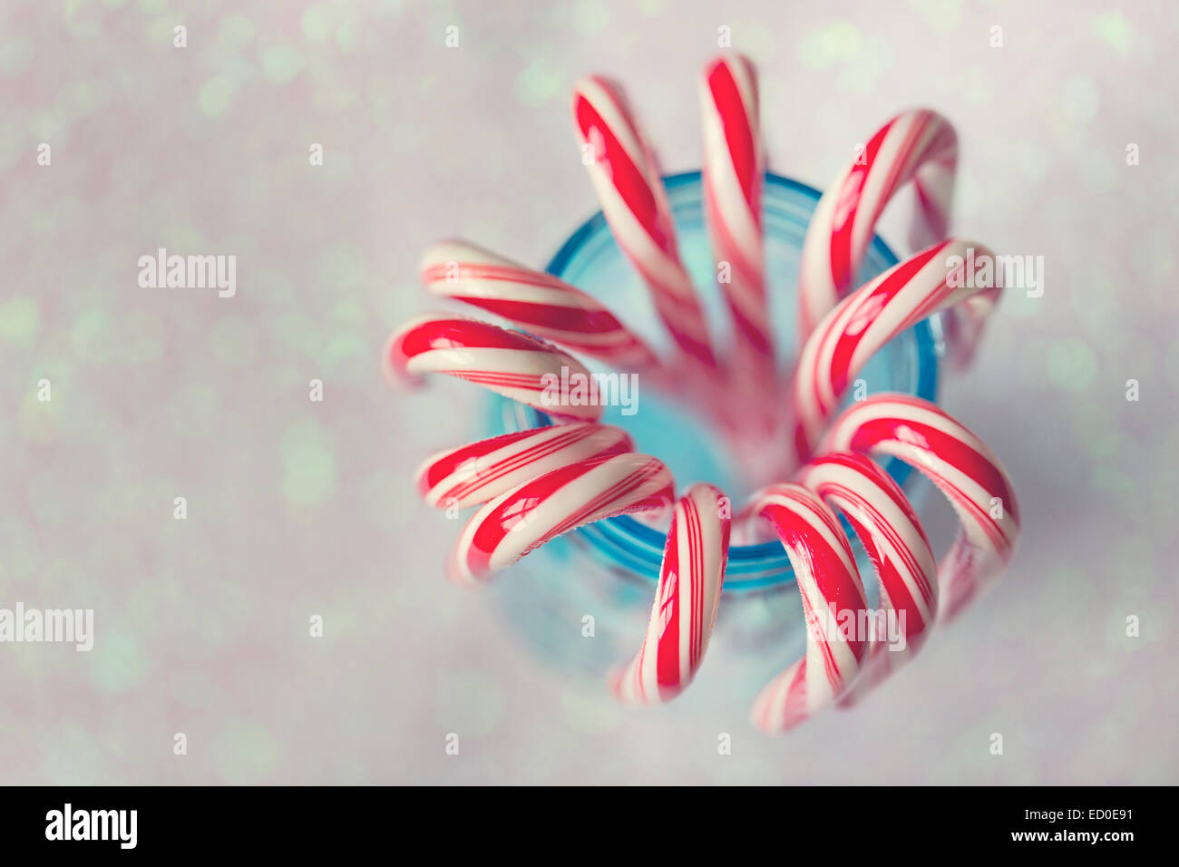 Red and white striped candy canes in blue mason jar against glittering background Stock Photo