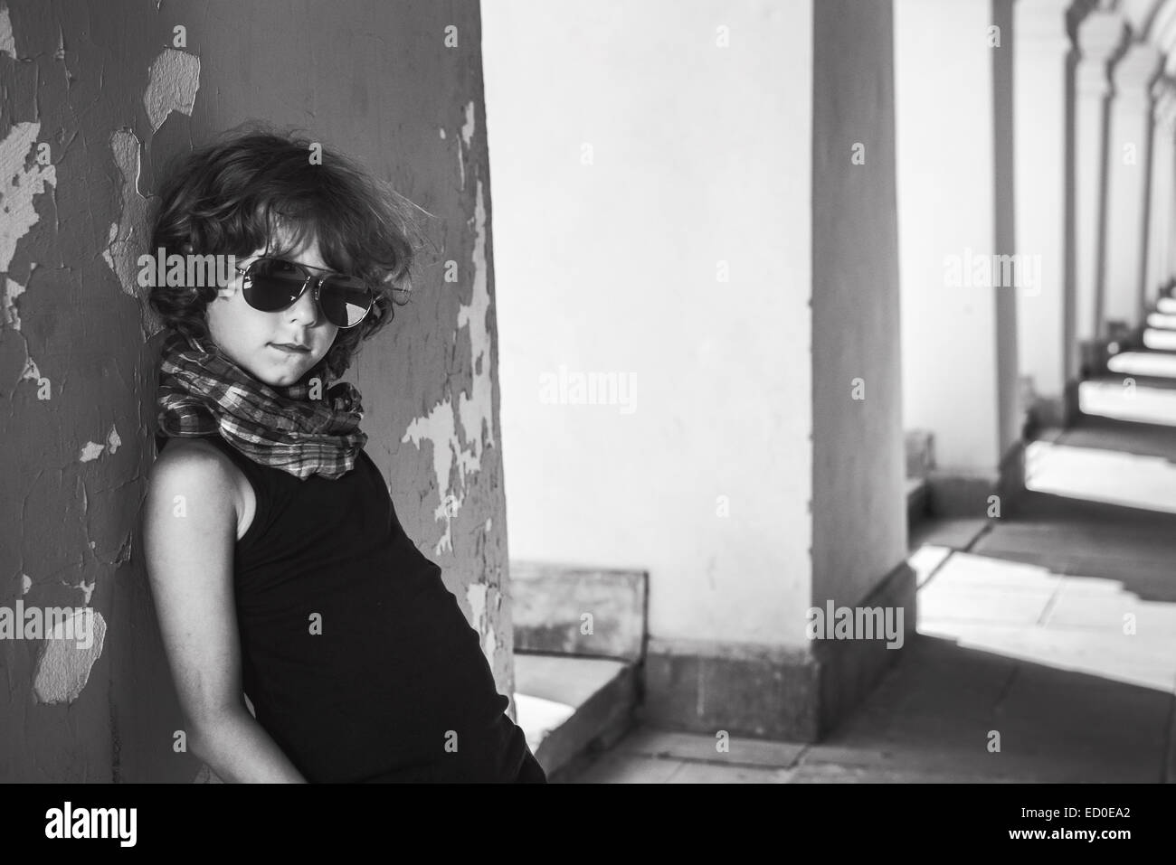 Boy (6-7) leaning against wall and looking at camera through sunglasses Stock Photo