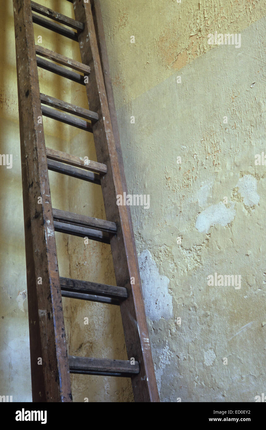 Set of two long wooden ladders leaning against corner of room with cream painted flaking rough plaster walls Stock Photo
