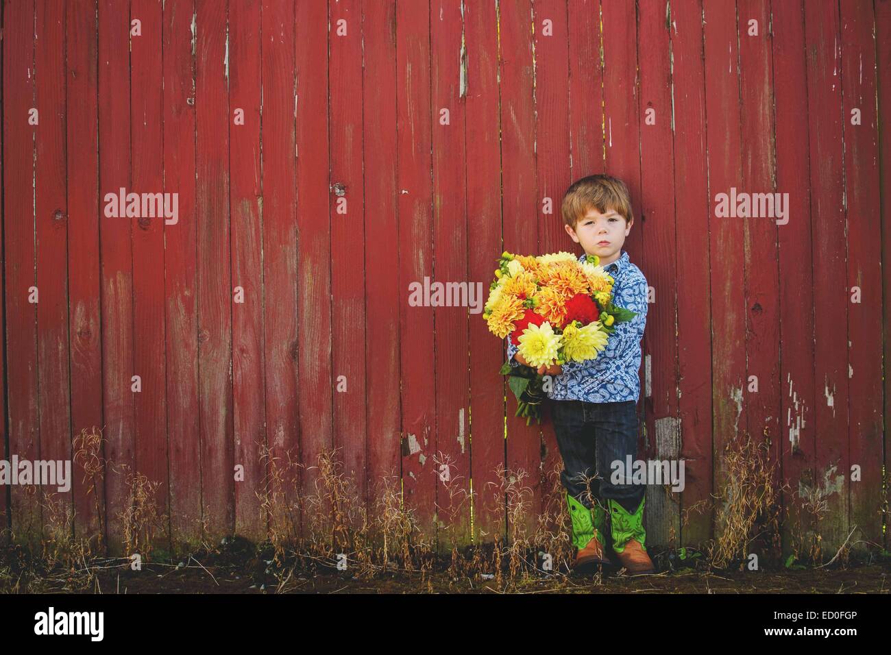 Boy standing in front of a red wall holding a bunch of flowers Stock Photo