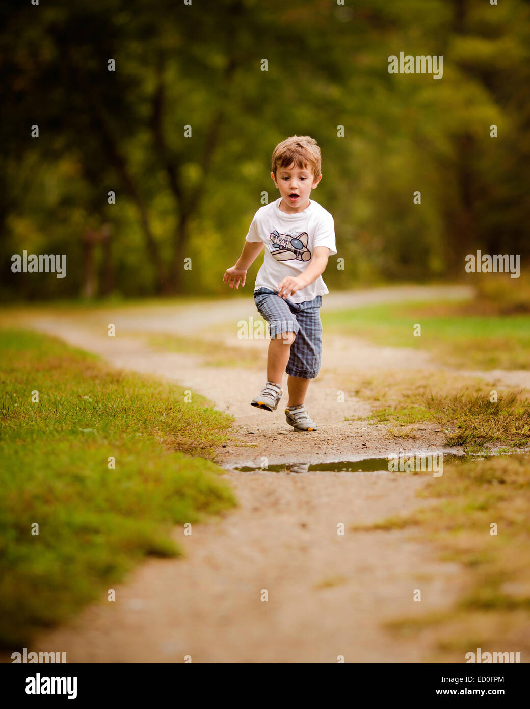 Boy running along footpath about to jump over a puddle Stock Photo