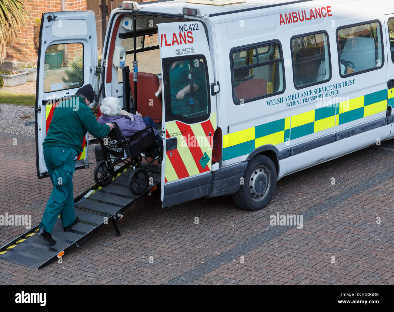 Welsh Ambulance NHS Trust patient transport service operator collecting an elderly patient in a wheelchair from home. Wales UK Stock Photo