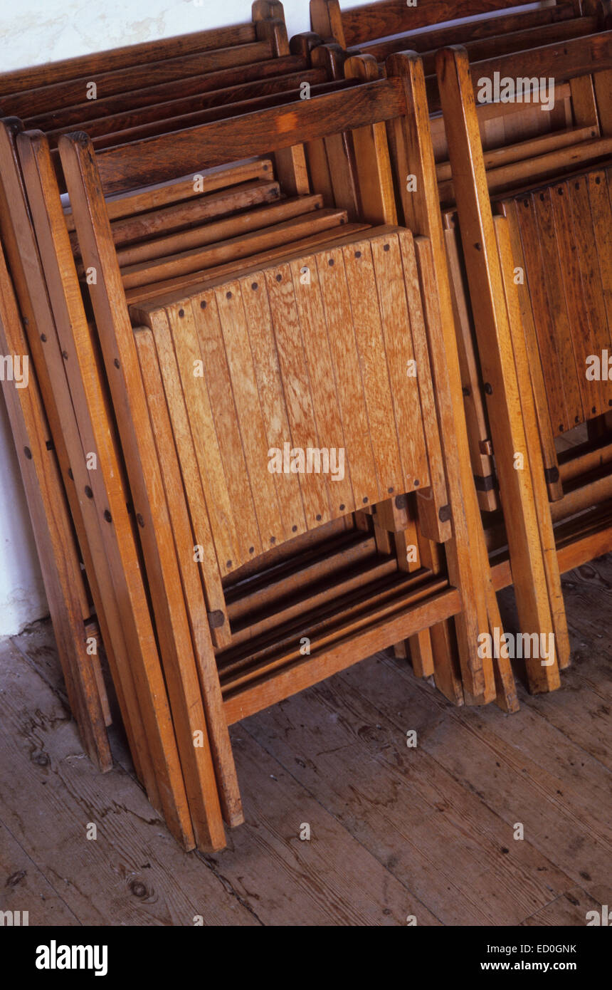 Wooden folding chairs stacked in two rows against white wall on plain