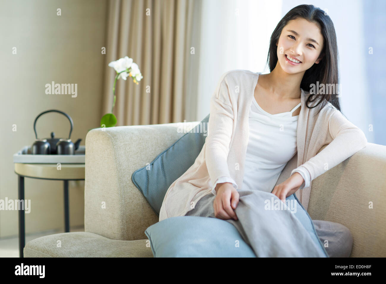 Happy young woman sitting on sofa Stock Photo - Alamy